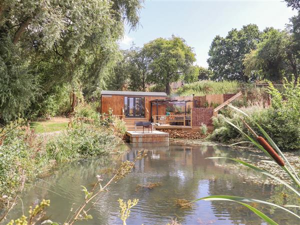 A shepherds hut of light wood colour with a raised deck over the water for fishing