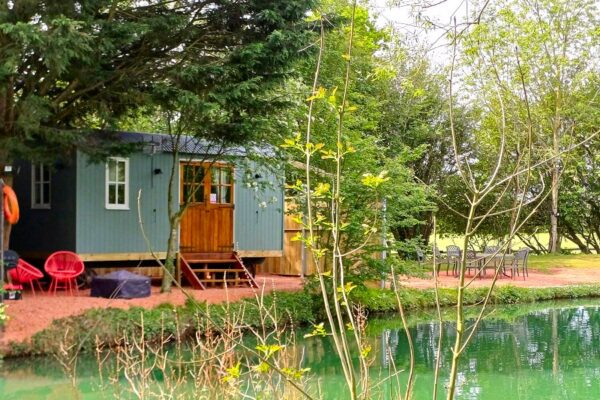 A teal green shepherds hott wuth wooden door and steps on a lakeside setting