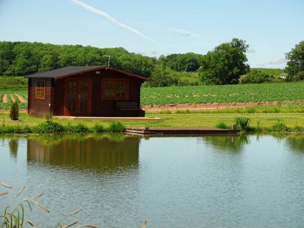 Country side cabins Herefordshire- a log cabin on the back of a calm lookin fishing lake with grass bank