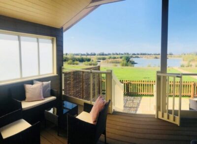 A lodge decking from the front door looking over a grass bank to the lake. (Waterside lodges Cambridgshire)