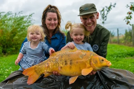 A family holding an orange mirror carp on the bank at Bearley Lakes, Somerset