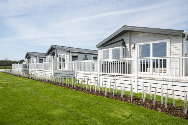 Row of cream lodges with white decking and lawns at Broadland Sands, Corton, Suffolk