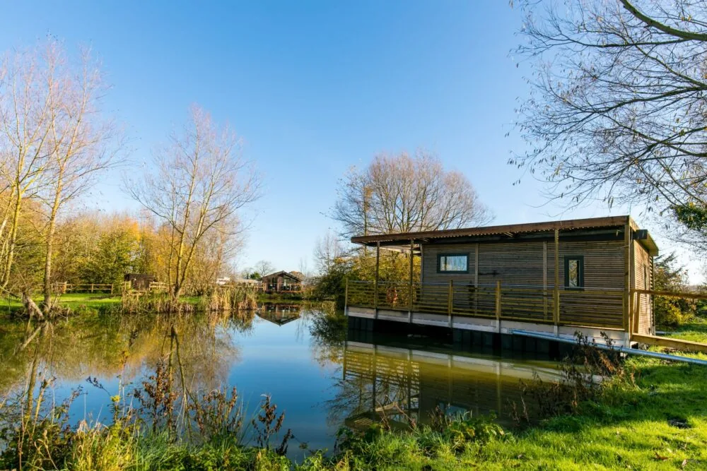 Timber fishing lodge with decking overhanging the bank of a still carp lake