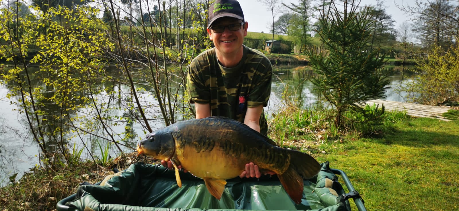 An angler holding a mirror carp beside the lake at Colehurst Lake Lodges & Glamping, Shropshire