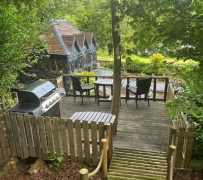 Raised timber decking with barbecue, table and chairs beside a lodge at Colehurst Lake Lodges & Glamping