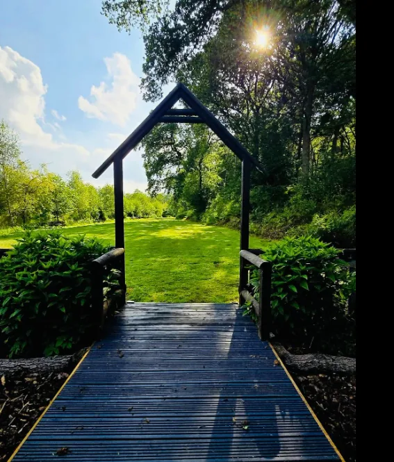 View from a lodge doorway across a decked walkway and timber archway to lawns at Colehurst Lake Lodges & Glamping