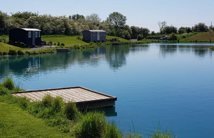 Two shepherds huts beside a blue lake with wooden fishing pegs at Cross Keys