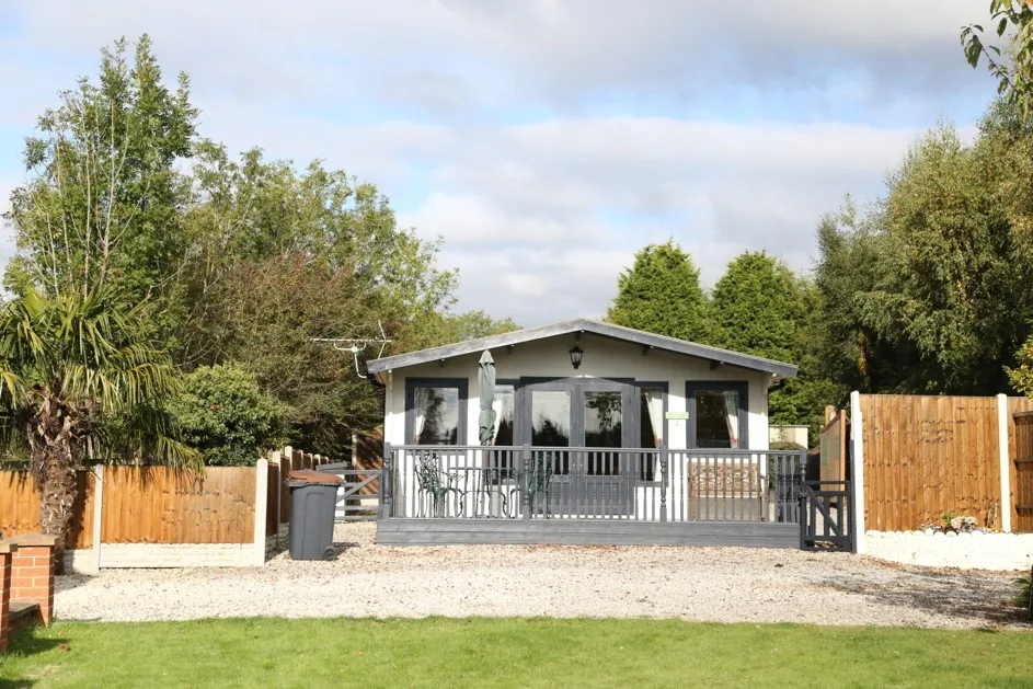 Modern grey and white holiday lodge with a railed decking veranda and gravel garden