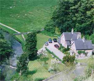 Aerial view of Dove Cottages, stone cottages in a green valley beside a river