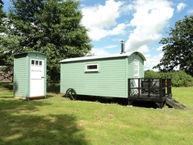 Sage green shepherds hut at Drove Lea with black raised decking and matching toilet cubicle