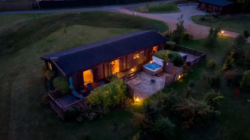 Aerial view of a timber lodge with a lit hot tub terrace at Fynn Valley Lodges, Suffolk