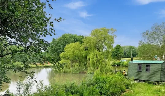 Shepherds hut beside a coarse fishing lake at Hastingford, with willows along the bank
