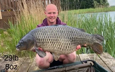 An angler kneeling on a wooden platform holding a large common carp at Head Fen Country Retreat