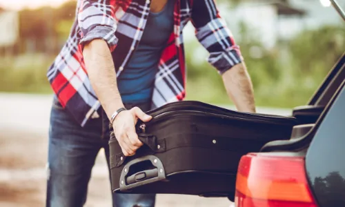 A man loading a suitcase into a car boot before a UK holiday