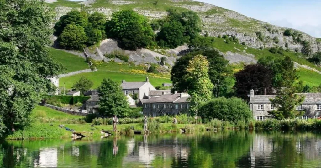 Anglers fly fishing on a lake below limestone crags at Kilnsey Park, Yorkshire Dales