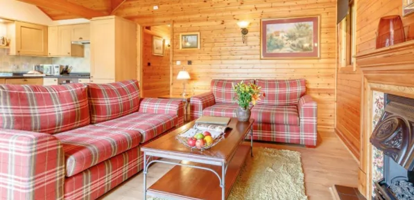 Pine clad lodge living room with tartan sofas, coffee table and fireplace