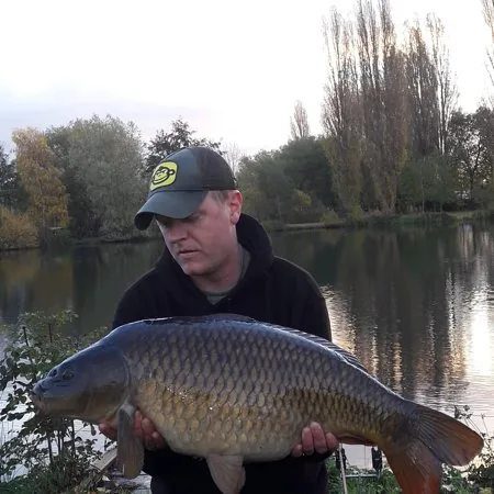 An angler holding a common carp beside a lake in West Norfolk