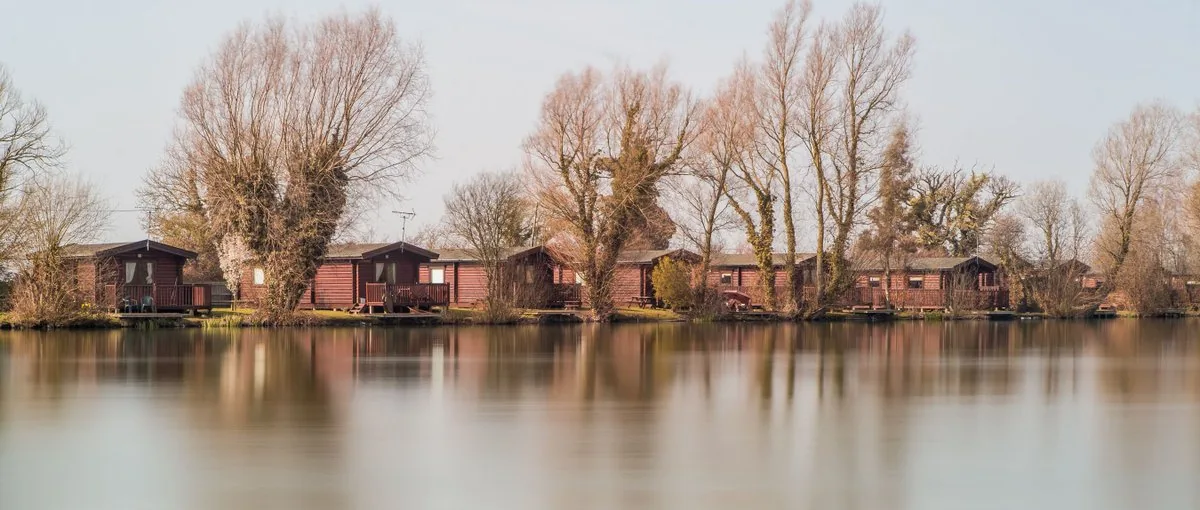 Row of timber log cabins with fishing pegs along a still lake shore