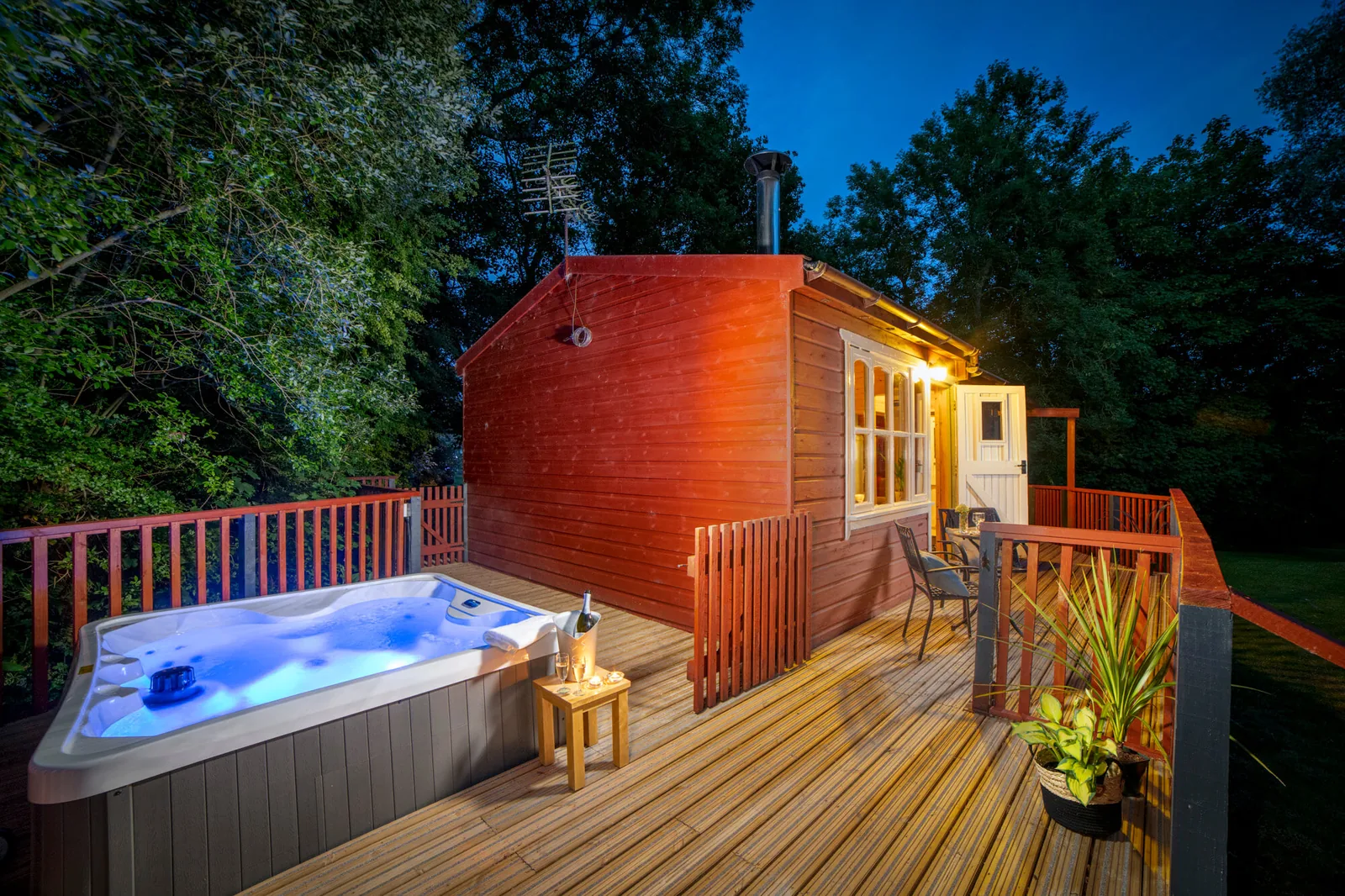Timber lodge at Otter Falls, Honiton, with a lit hot tub on the decking at dusk