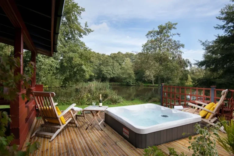 Hot tub and deck chairs on a lodge deck overlooking the lake at Otter Falls, Honiton