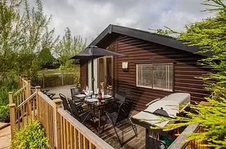 Timber lodge with decked terrace, parasol dining set and hot tub beside a private fishing lake
