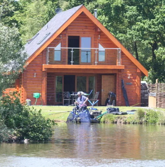 Two storey timber fishing lodge with an angler fishing from a private peg on the lake bank