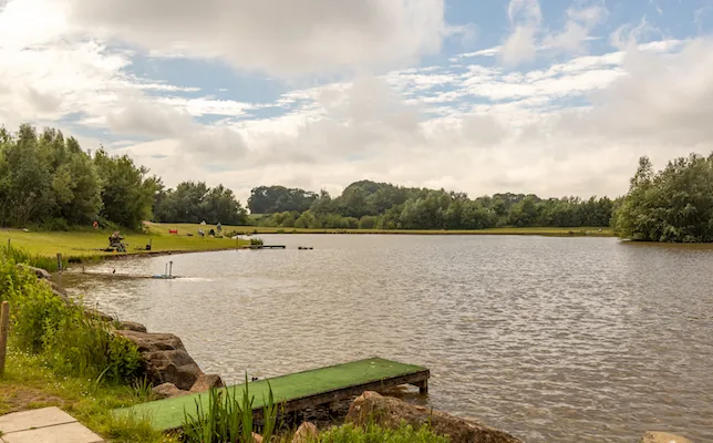 Coarse fishing lake with wooden platform and anglers at Stanley Villa Farm, Lancashire
