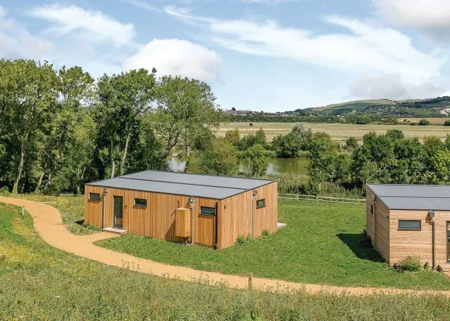 Timber lodges on a grassy slope above the lake at Swanborough Lakes, Lewes