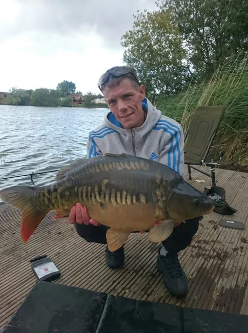 An angler on a wooden platform holding a mirror carp at Tattershall Lakes, Lincolnshire