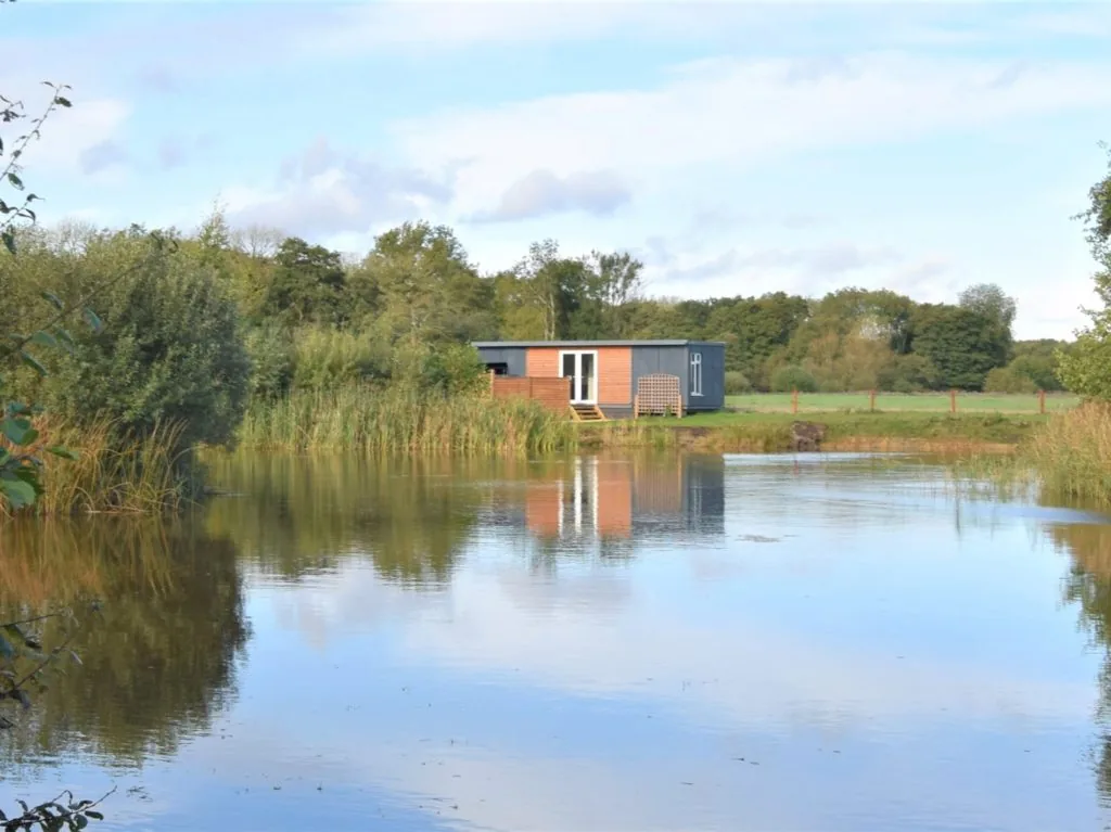 Lakeside pod at The Lily Pad in Norfolk reflected in a still fishing lake