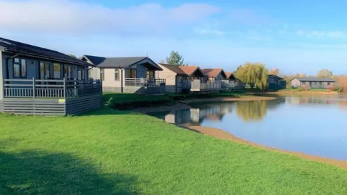 Row of lakeside lodges with decking beside a grass banked fishing lake at Willow Lakes, Lincolnshire