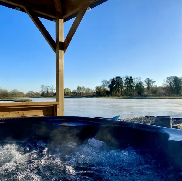 Bubbling hot tub under a timber canopy looking out over a large lake